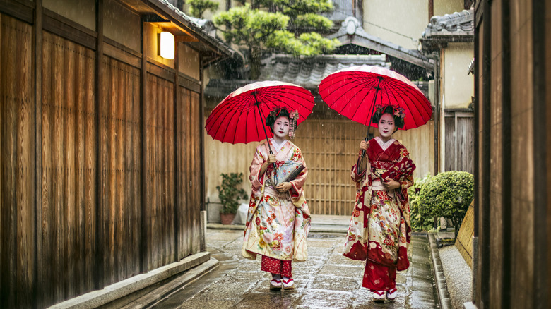 Deux femmes en kimono japonais traditionnel portant des parapluies rouges dans une ruelle