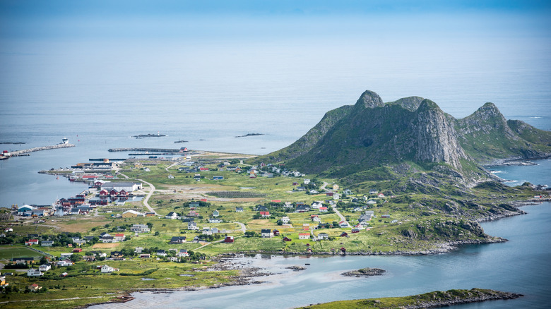 Un large tir aérien regardant toute l'île de Vaeroy avec de petites maisons sur une plaine plate à côté de hautes montagnes arrondies
