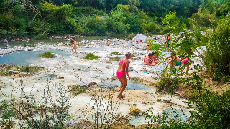 Une jeune femme en maillot de bain rose se dirige vers une source chaude avec d'autres visiteurs