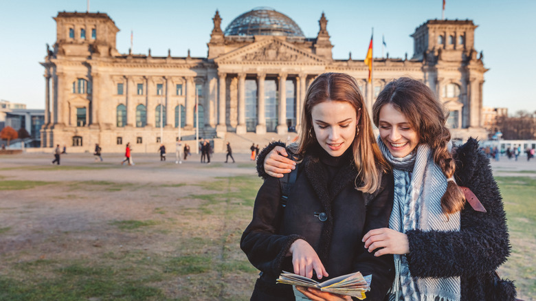 Femme souriant avec un bras autour de la deuxième femme alors qu'ils lisent tous les deux une carte devant le bâtiment du Reichstag de Berlin