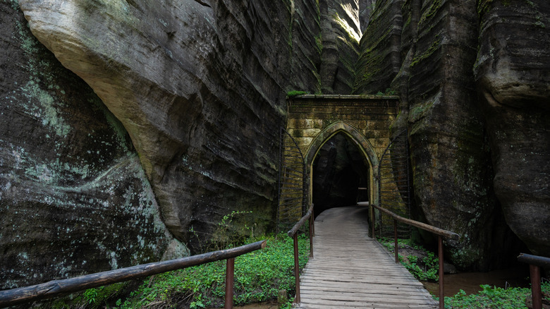 Porte en pierre et passerelle en bois menant à la formation de roche caverneuse