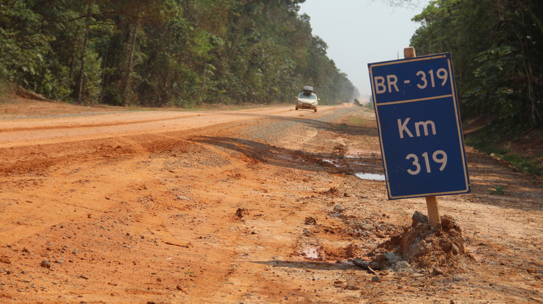 Un panneau marquant le BR-319 sur un chemin de terre avec une voiture approchant en arrière-plan