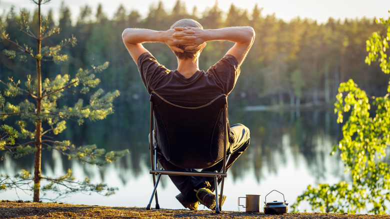 L'homme se détend dans la chaise de camp par lac boisé en Suède