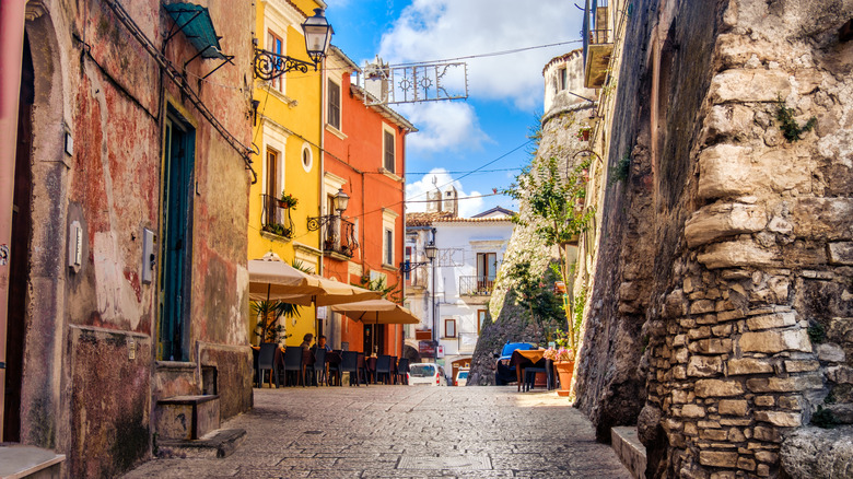 Petite ruelle à Vico del Gargano, en Italie avec de vieux bâtiments en pierre qui bordent la passerelle et trois parapluies à l'extérieur d'un restaurant.