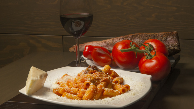 Une assiette de rigatoni all'amatriciana à côté des tomates et des piments et un verre de vin