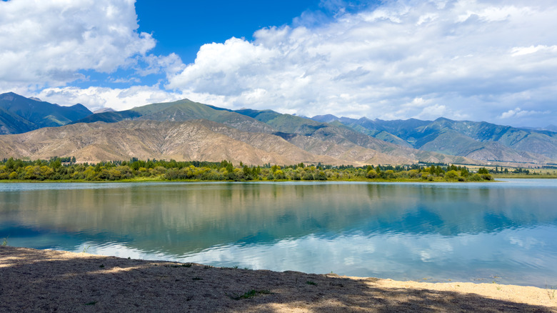 Une photo de la surface calme du lac par une journée ensoleillée reflétant les montagnes