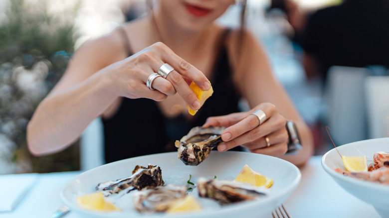 Section intermédiaire de femme mettant du citron sur une huître dans un restaurant en France