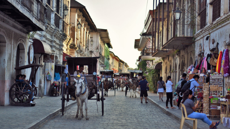 Vue dans la ville de Vigan City avec des voitures et des gens dessinés des chevaux des deux côtés de la rue.