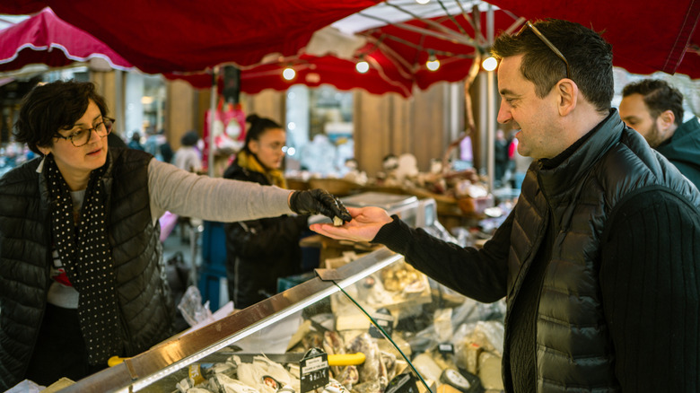 Un homme échantillonne le fromage d'un vendeur sur un marché français
