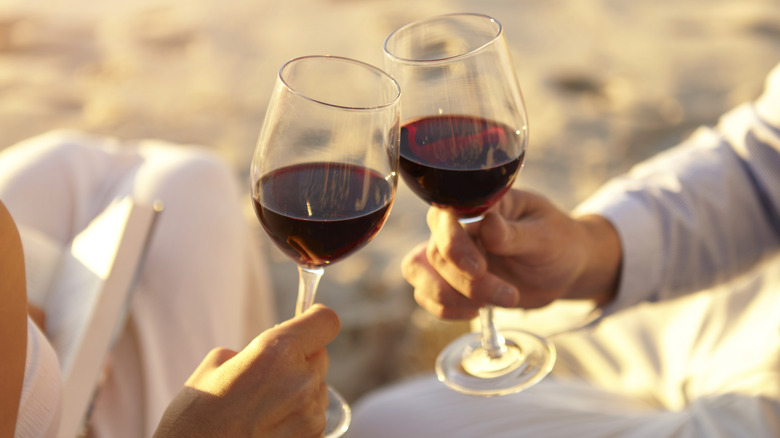 Deux personnes à l'extérieur touchant des verres de vin rouge