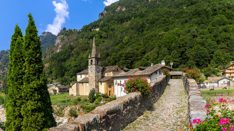 Une vue pittoresque d'un pont en pierre historique menant à une église et à des maisons entourées de montagnes et de fleurs dans la vallée d'Aosta, en Italie