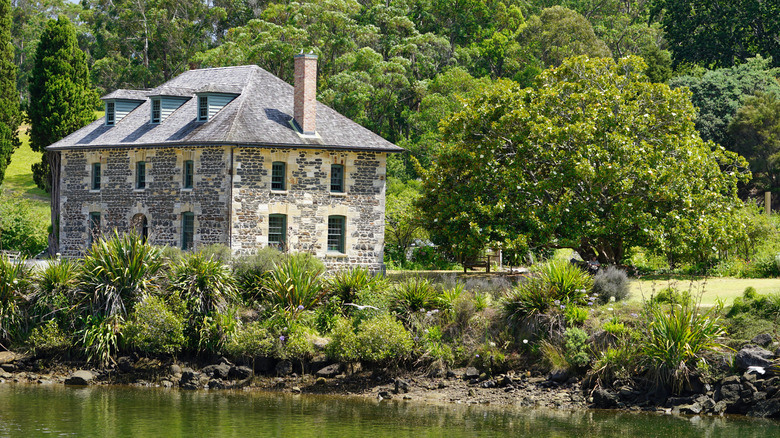 Le magasin en pierre historique de Kerikeri entouré d'arbres verts et à côté de l'eau
