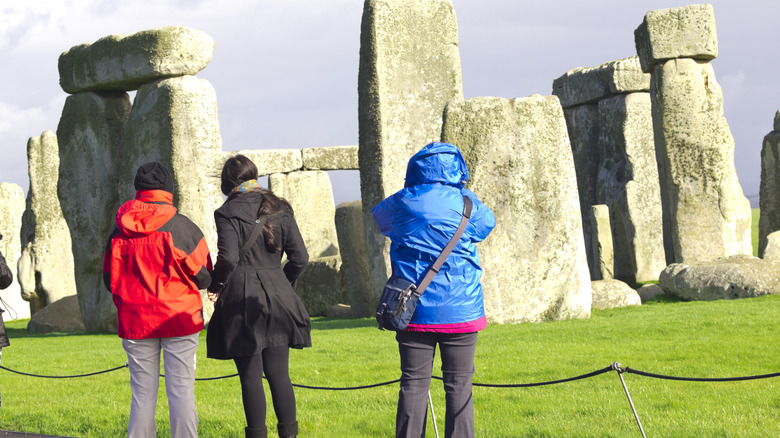 Les gens prenant des photos de Stonehenge de la piste de randonnée derrière une barrière de corde