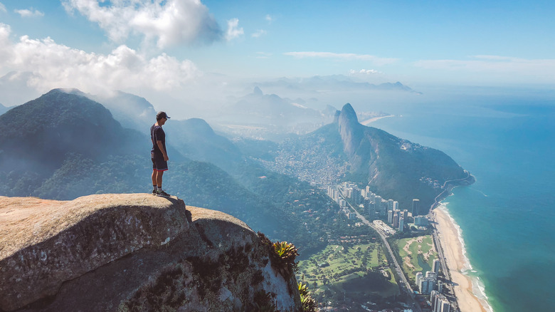 Un homme se tient au sommet d'une falaise en bord de mer, regardant vers le bas sur une plage à Rio