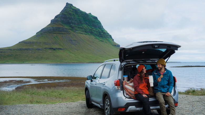 Couple assis sur un coffre en voiture ouvert lors d'une pause-voyage en Islande