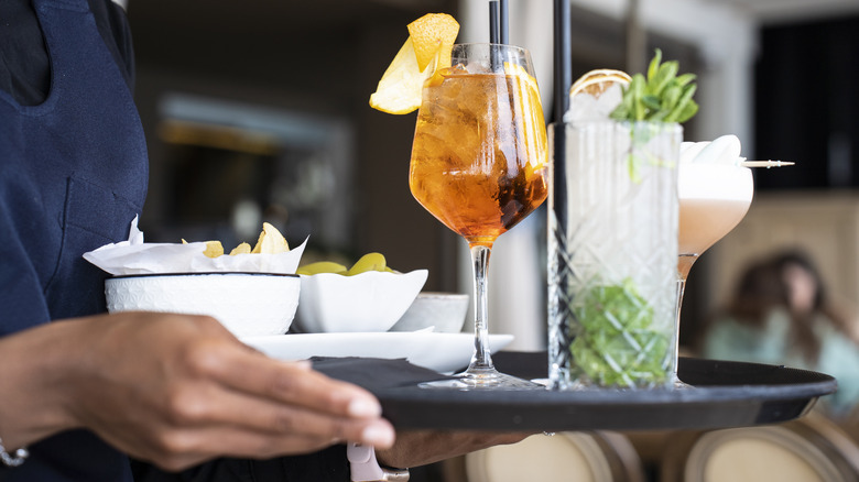 Les mains d'un serveur portent un plateau plein de collations et de cocktails
