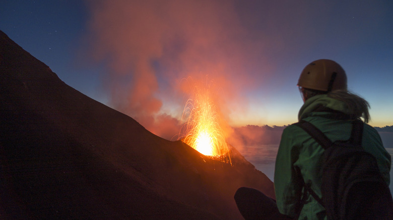 Randonneur avec un casque regarde l'éruption volcanique au mont Stromboli