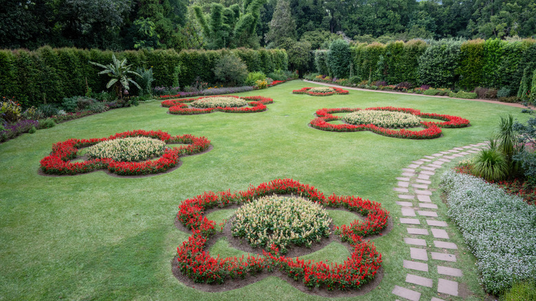 Une pelouse ornementale verte présente des parterres de fleurs en forme de fleurs rouges avec des centres jaunes