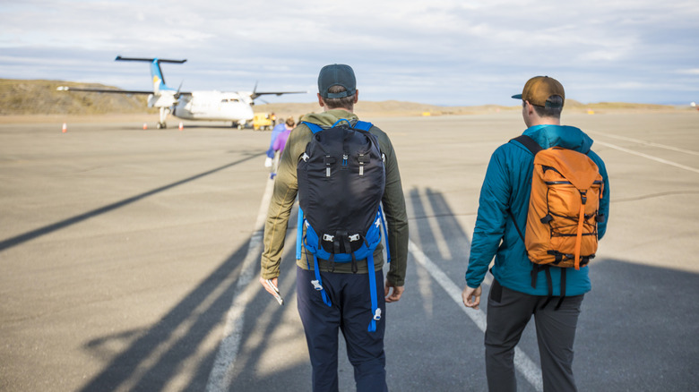 Deux routards sur un tarmac marchant vers un petit avion.