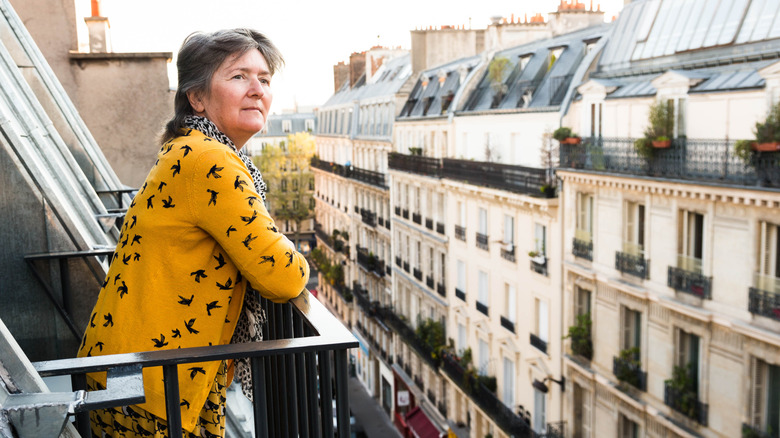 Femme plus âgée debout sur un balcon sur une rue à Paris
