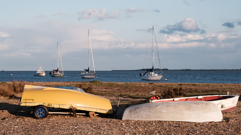 Une vue sur les voiliers en mer au large de l'île de Mersea avec des bateaux de pêche à l'envers sur la plage au premier plan