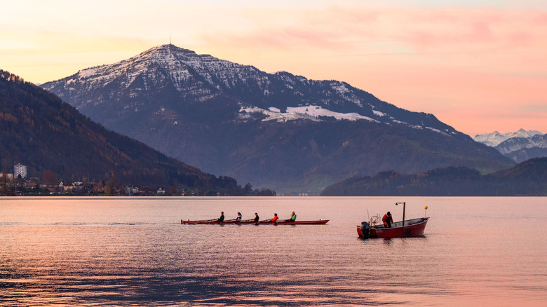 Un coucher de soleil derrière une montagne enneigée sur le lac Zug avec des rameurs et un pêcheur