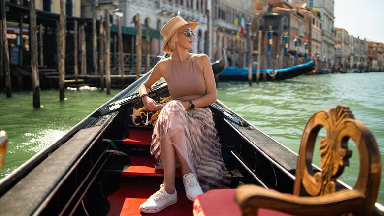 Une femme dans un chapeau et une jupe assise dans une gondole à Venise, en Italie.