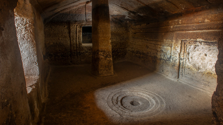 Chambre intérieure d'un Domus de Janas avec une colonne en pierre et des cercles concentriques gravés dans le sol