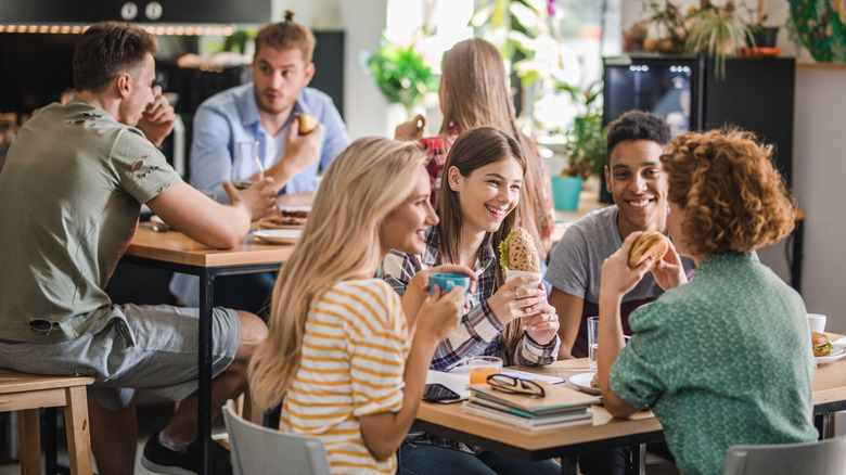 Étudiants universitaires souriant et assis autour d'une table de cafétéria UNI déjeunant.