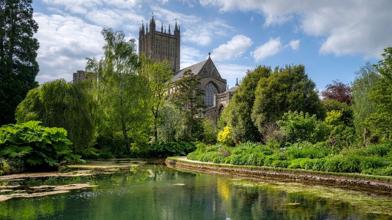 Cathédrale de Wells entourée de verdure luxuriante et d'un étang tranquille sous un ciel partiellement nuageux à Somerset, en Angleterre