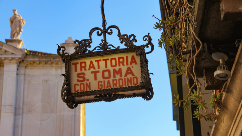 Un panneau pour une trattoria est suspendu au-dessus d'une rue à Venise, en Italie