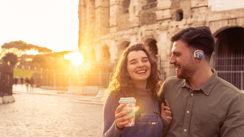 Un couple itinérant souriant et buvant du café alors qu'ils visitent la ville près du Colisée à Rome, en Italie.