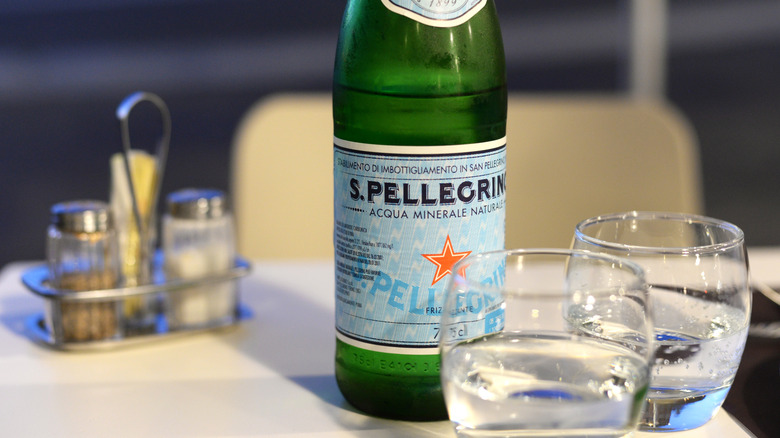 Une bouteille de San Pellegrino est ouverte avant deux verres d'eau sur une table de lin blanche avec du sel et du poivre