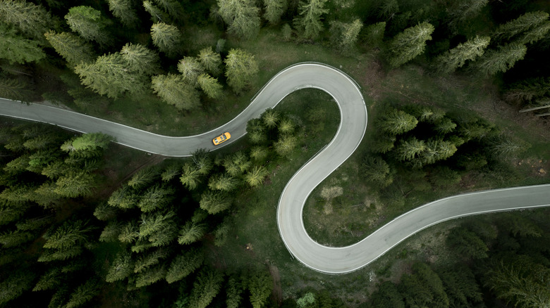 Une voiture peut être vue naviguer sur une route en forme de S à travers une région rurale et alpine d'Italie