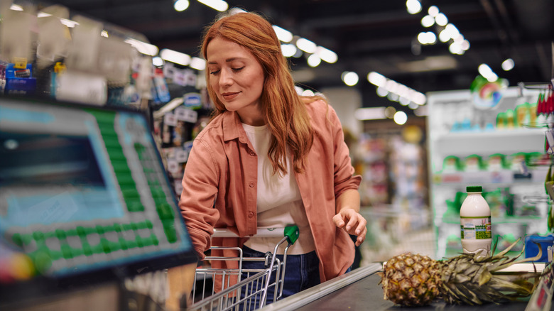 Une femme déchargeant son épicerie sur un tapis roulant de supermarché
