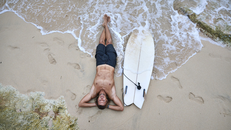 Surfeur allongé sur du sable à côté d'une planche de surf