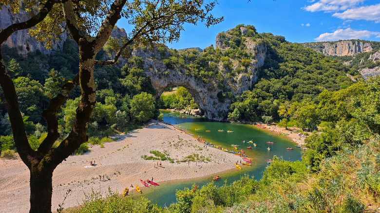 Rivière avec des kayakers sous une arche de pierre naturelle, entourée de verdure luxuriante près de Vals-les-Bains