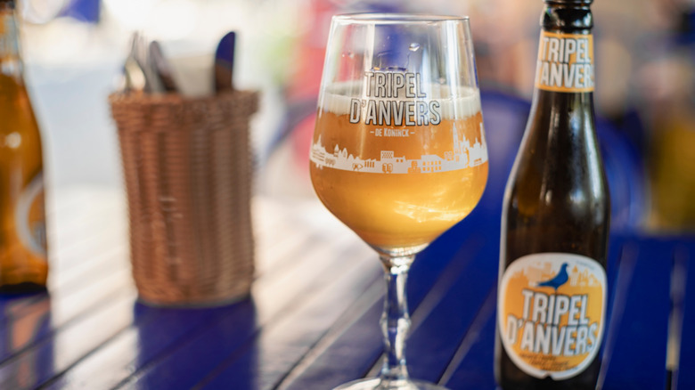 Une bière belge dorée dans un verre à côté de sa bouteille sur une table bleue