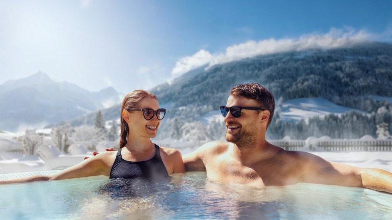 Un couple se détendant dans un bain à remous avec des montagnes enneigées derrière eux
