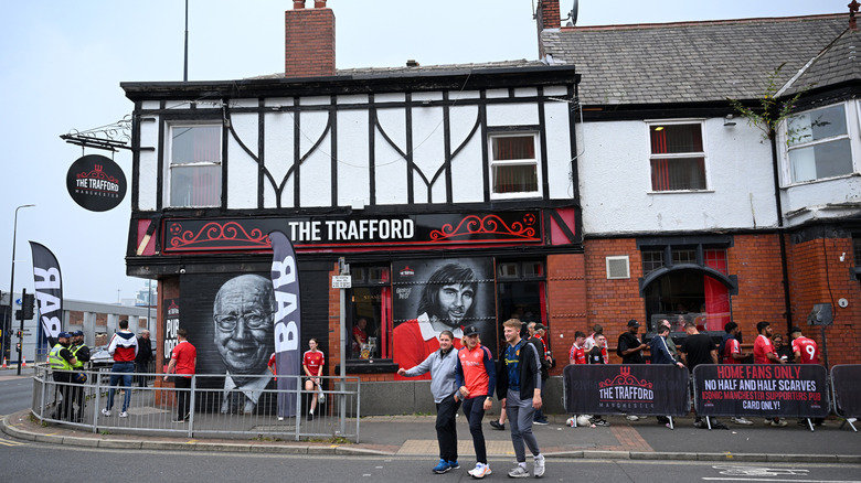 Le pub Trafford à Manchester avec des peintures murales de footballeurs sur le mur extérieur. Les fans sont autour du bâtiment et flânent sur la route.