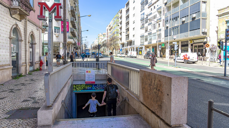 Un homme et un garçon entrant dans la station de métro Anjos avec des magasins et des appartements à proximité.