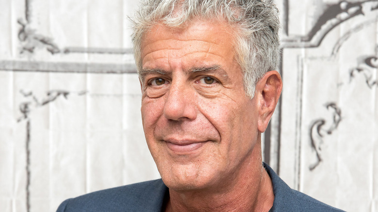 Anthony Bourdain regarde de côté petit sourire fond blanc