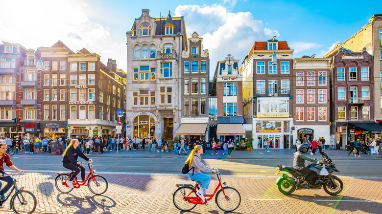 Cyclistes, piétons et automobilistes en scooter se déplaçant dans les rues d'Amsterdam face à l'architecture emblématique de la ville