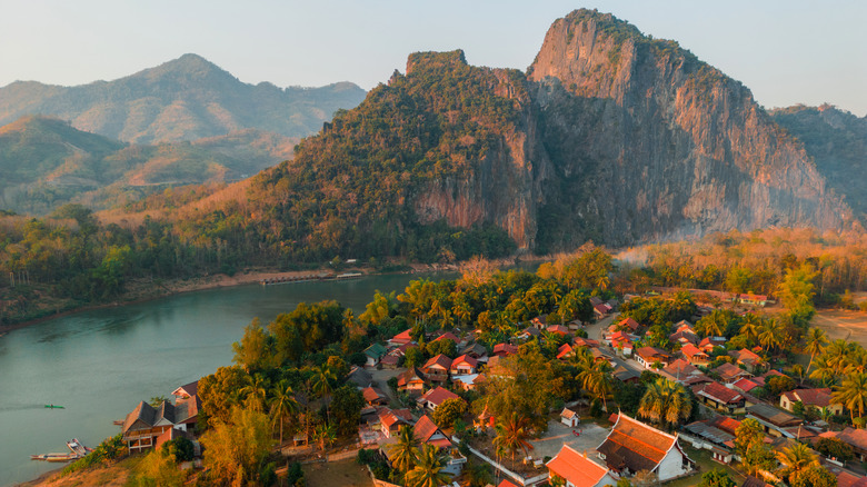 Un village aux maisons concaves aux toits rouges en pente, entouré par la jungle. Elle est séparée des montagnes par une rivière sinueuse.