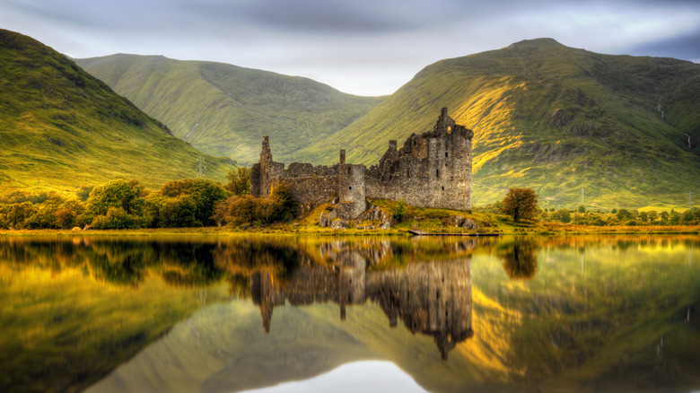 Les vestiges du château de Kilchurn, reflétés à la surface d'un lac avec des montagnes en arrière-plan