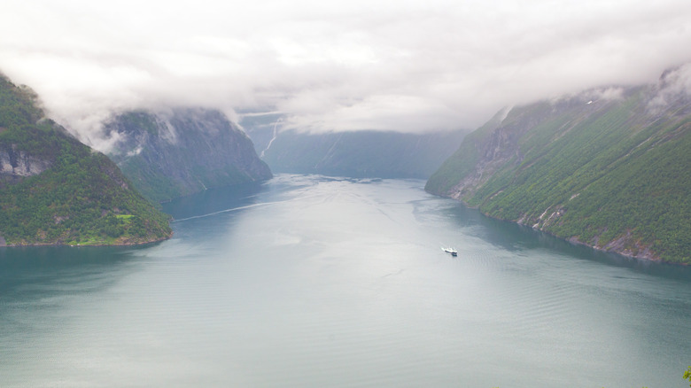 Journée nuageuse à Hornindalsvatnet en Norvège, avec une personne naviguant dans l'eau entourée de montagnes