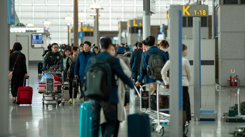 Passagers marchant le long d’un couloir d’aéroport à côté des comptoirs d’enregistrement