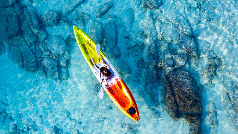 Vue de dessus d'un kayakiste ramant sur des eaux bleu clair avec du sable et des rochers