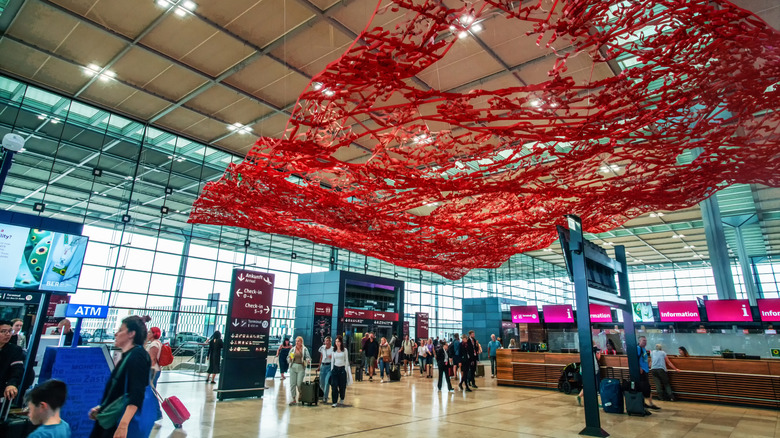 Intérieur de l'aéroport de Berlin Brandebourg avec des voyageurs marchant et des œuvres d'art rouges au plafond