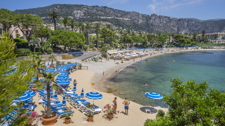 Plage des Fourmis à Beaulieu-sur-Mer, Côte d'Azur, avec palmiers et parasols bleus et blancs